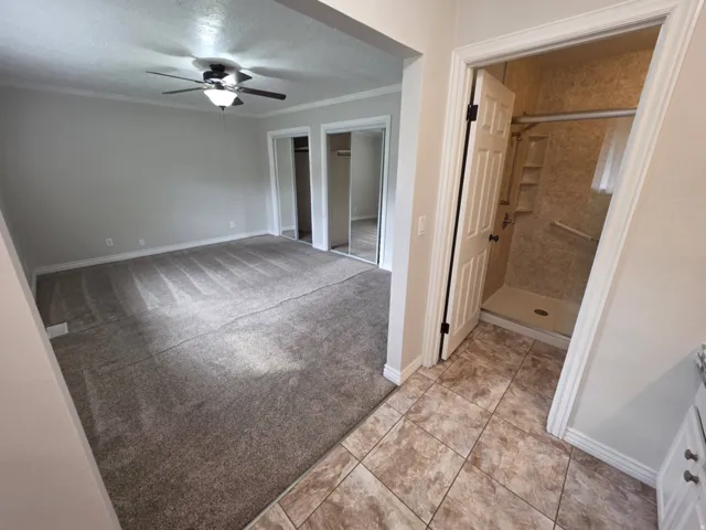 Spacious room with gray carpet flooring, ceiling fan with integrated lighting, and mirrored closet doors