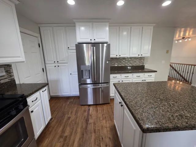 White cabinetry with dark hardware, stainless steel refrigerator, dark wood-finish flooring, and speckled dark countertops