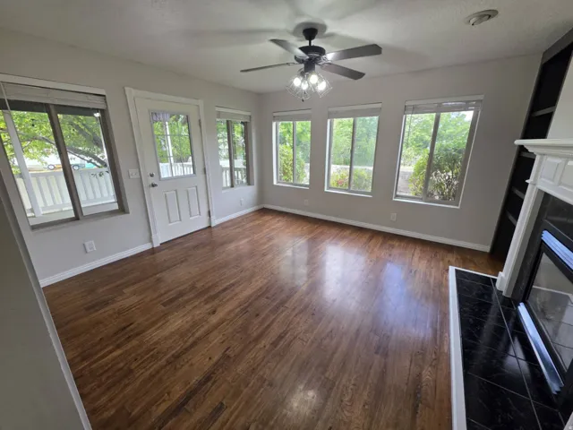 Wood-finish flooring, multiple windows, built-in shelving, fireplace with tile surround, and a ceiling fan with integrated lighting