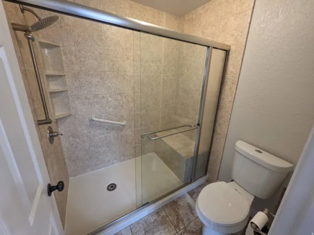 Glass-enclosed shower with a built-in bench, integrated shelving, and a rain showerhead