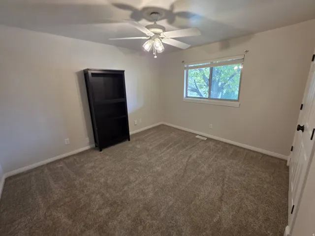 Neutral-toned carpeting, ceiling fan with integrated lighting, natural light from a double-paned window, and a white paneled door with black hardware