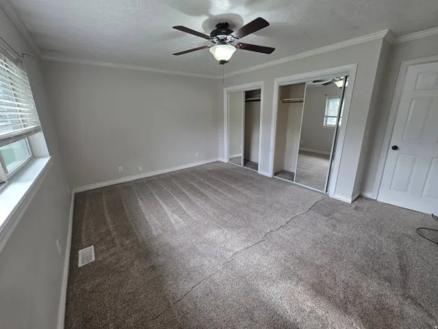Wall-to-wall carpeting, window with blinds, ceiling fan with integrated lighting, and mirrored closet doors