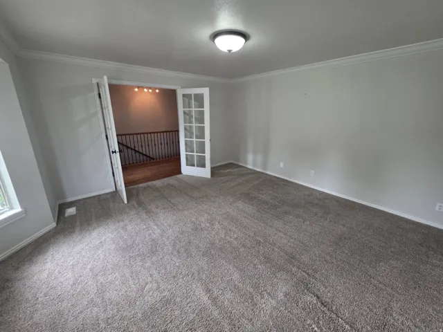 Carpeted room with crown molding, double French doors, and a semi-flush mount ceiling fixture