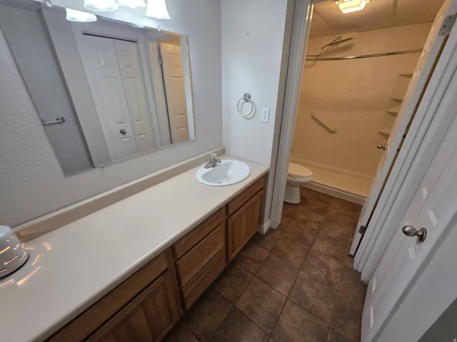 Bathroom featuring a vanity with an integrated sink, wood-finish cabinetry, a large wall mirror, and a shower with built-in shelving