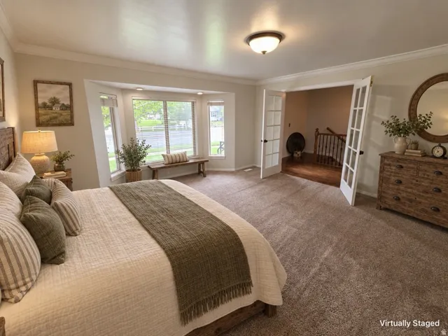 Bay window with integrated seating, carpeted flooring, white French doors, ceiling-mounted light fixture, and wood-finish dresser with drawer pulls