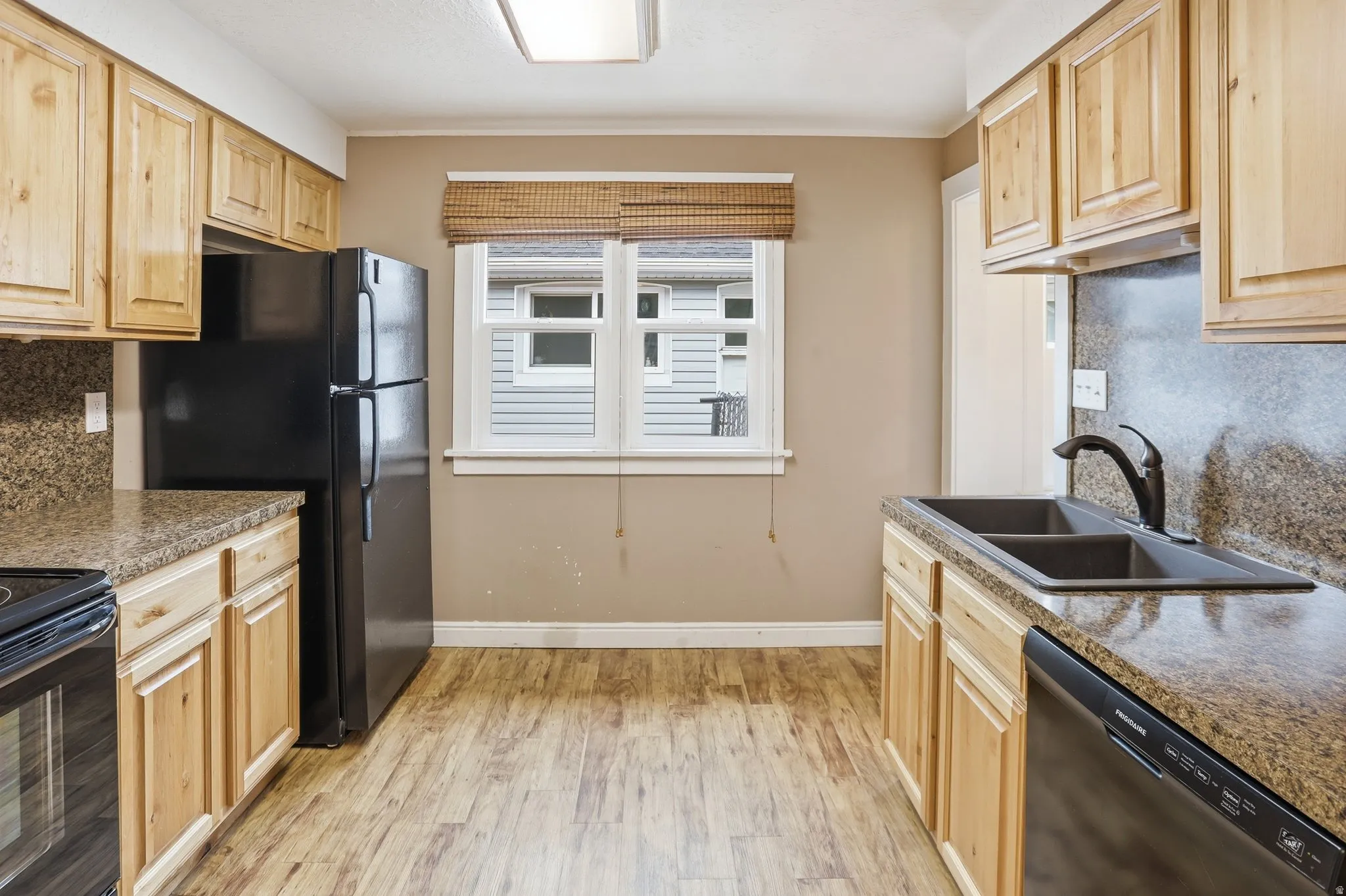 Kitchen featuring wood-finish cabinetry, black appliances, a double basin sink, and wood-finish flooring