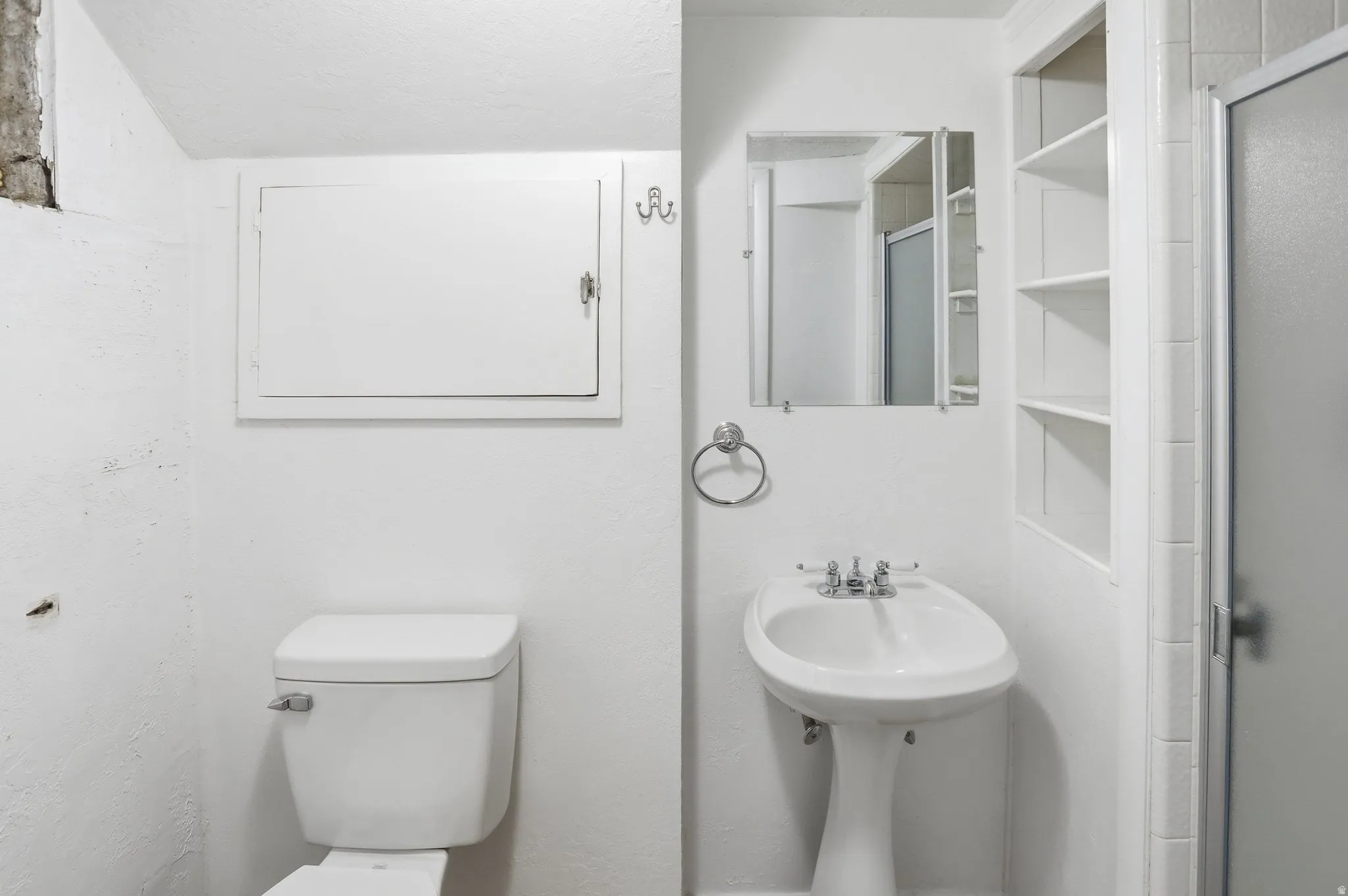 Pedestal sink with chrome fixtures, wall-mounted mirror, and built-in shelving