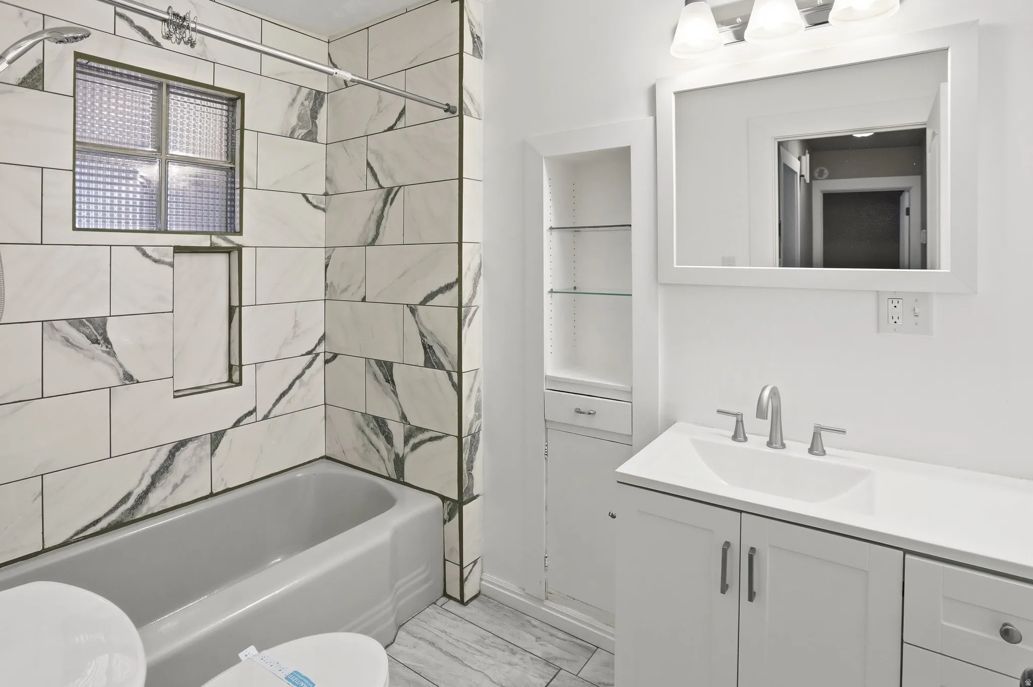 Bathtub with subway tile surround, integrated shower niche, and a privacy window