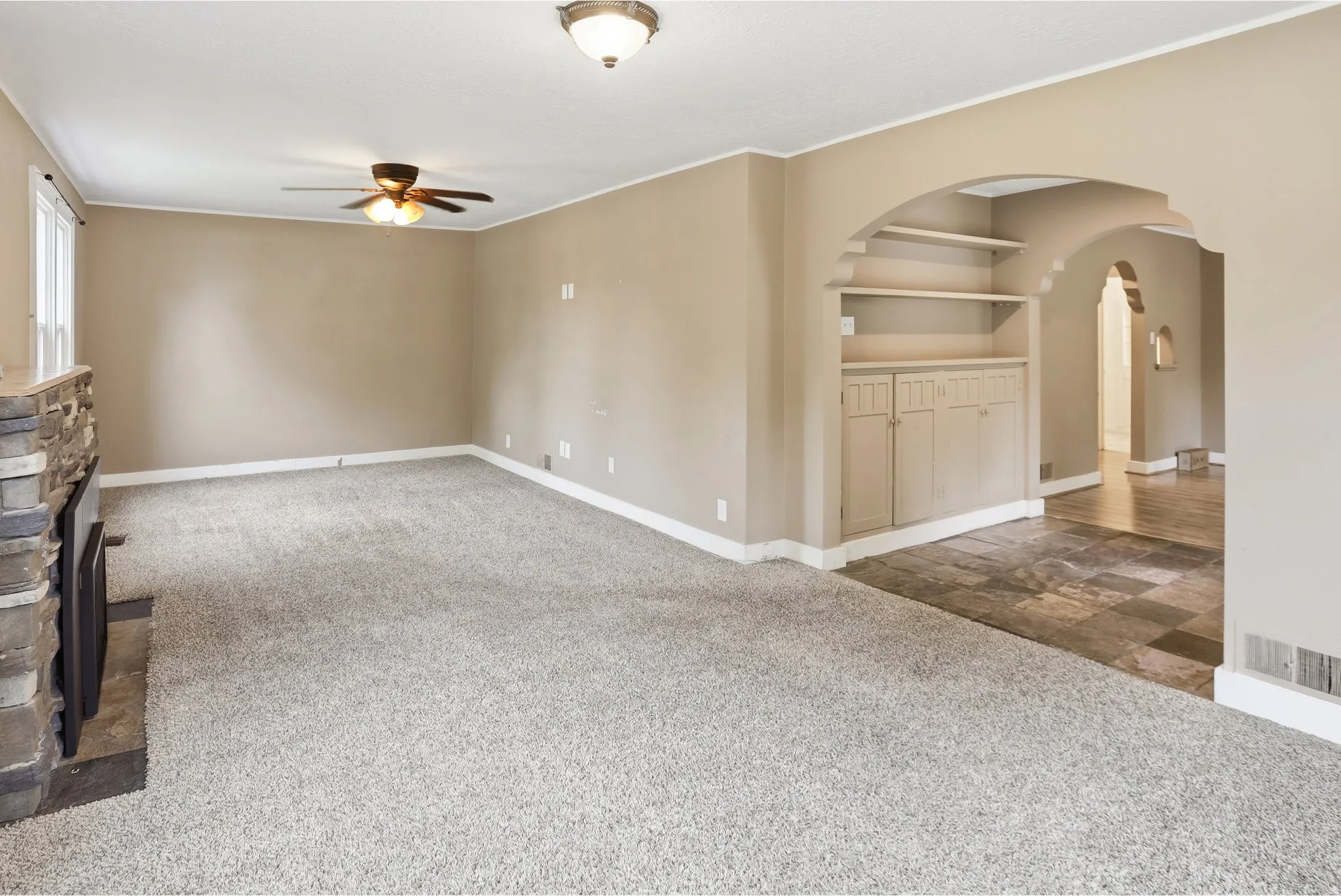 Built-in shelving with cabinetry, archways, stone fireplace, ceiling fan, and recessed lighting