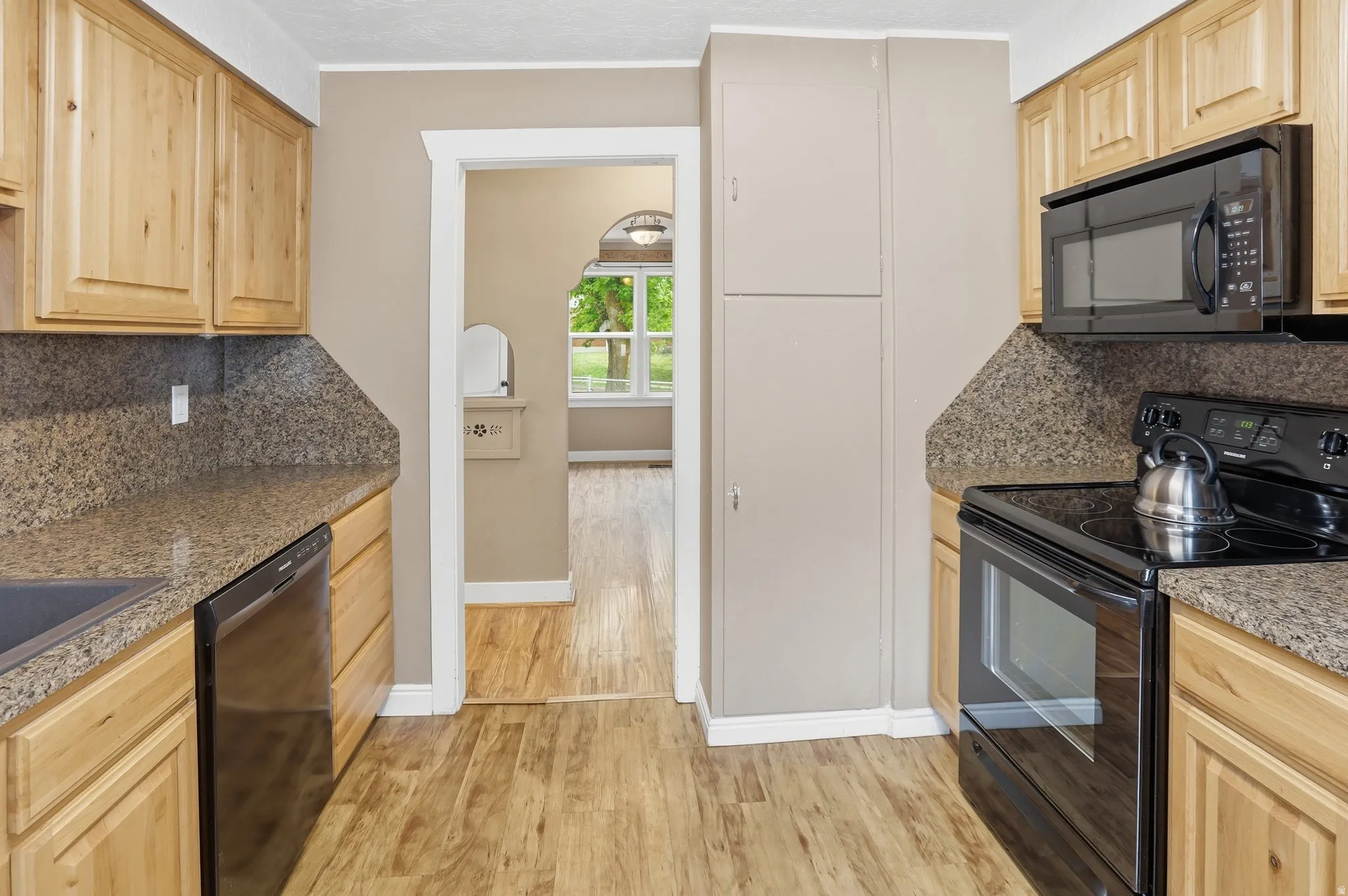 Wood-finish flooring with light wood cabinetry, stone-patterned countertops, and black built-in appliances
