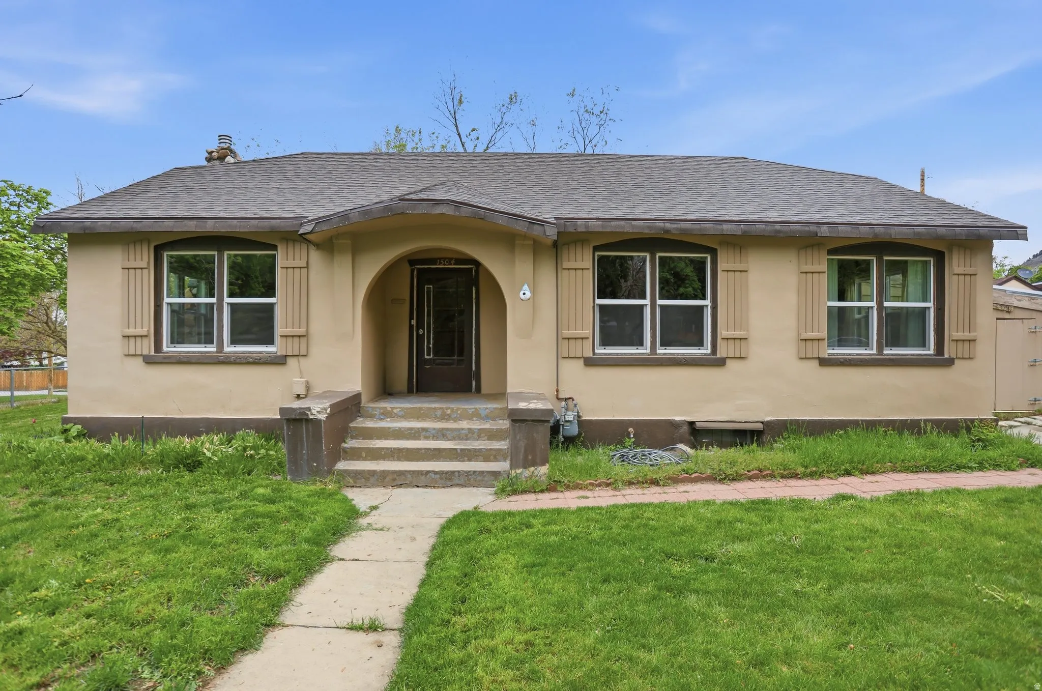 Stucco exterior featuring arched entry, stone steps, a dark wood-finish entry door, and decorative window shutters