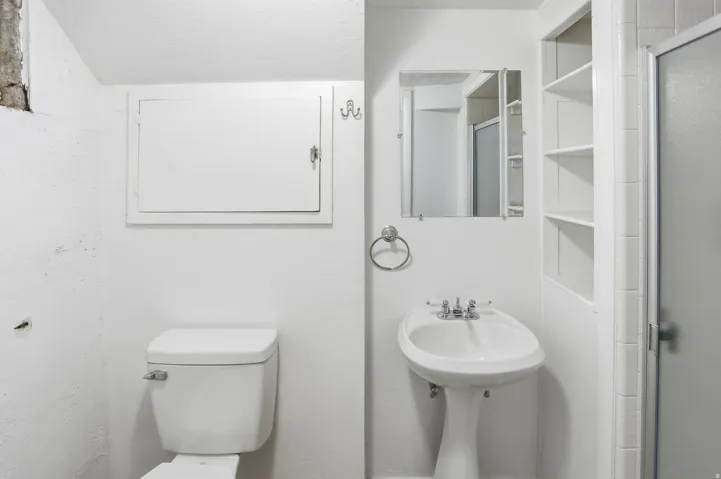 Pedestal sink with chrome fixtures, wall-mounted mirror, and built-in shelving