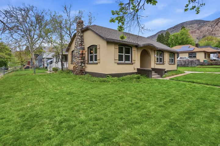 Stucco exterior with a stone chimney, covered entry, and multiple windows
