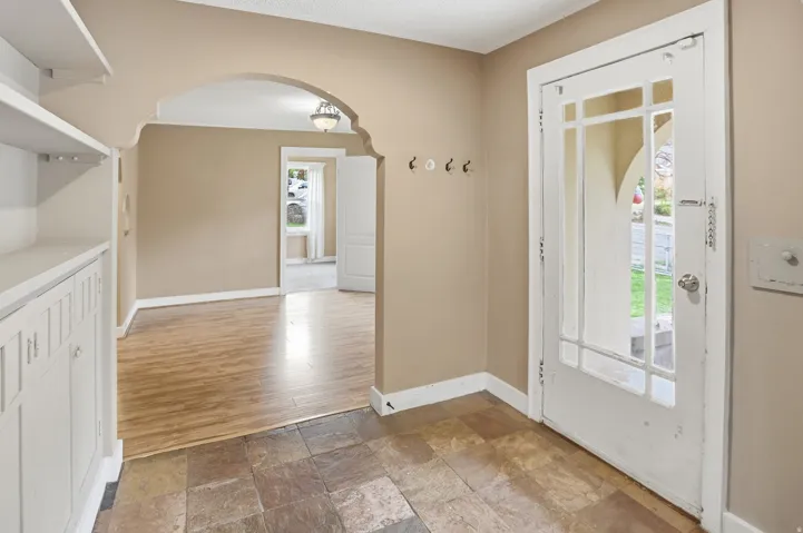 Entryway with slate tile flooring, a glass-paned door, and an arched doorway leading to wood-finish flooring