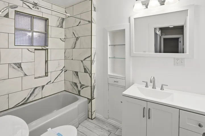 Bathtub with subway tile surround, integrated shower niche, and a privacy window