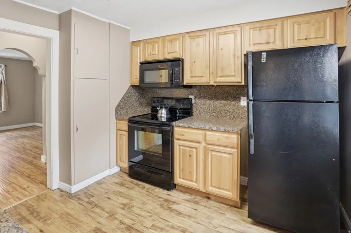 Kitchen featuring wood-finish flooring, light wood cabinetry, black appliances, and speckled countertops