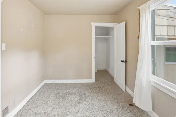 Textured carpeting with light neutral wall tones, a double-hung window, and an open closet with interior shelving