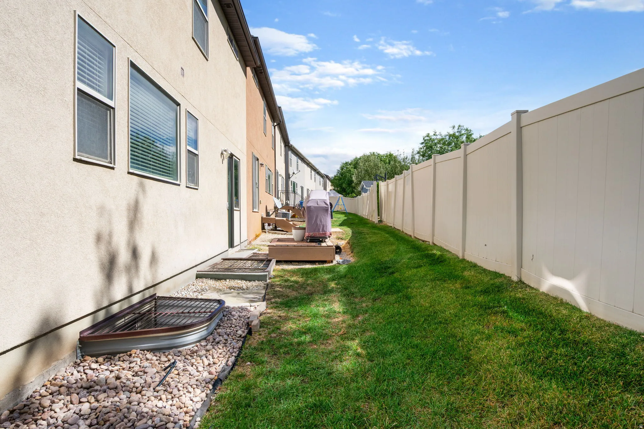 Stucco exterior, multiple windows, basement window well, vinyl fencing, and a grassy perimeter