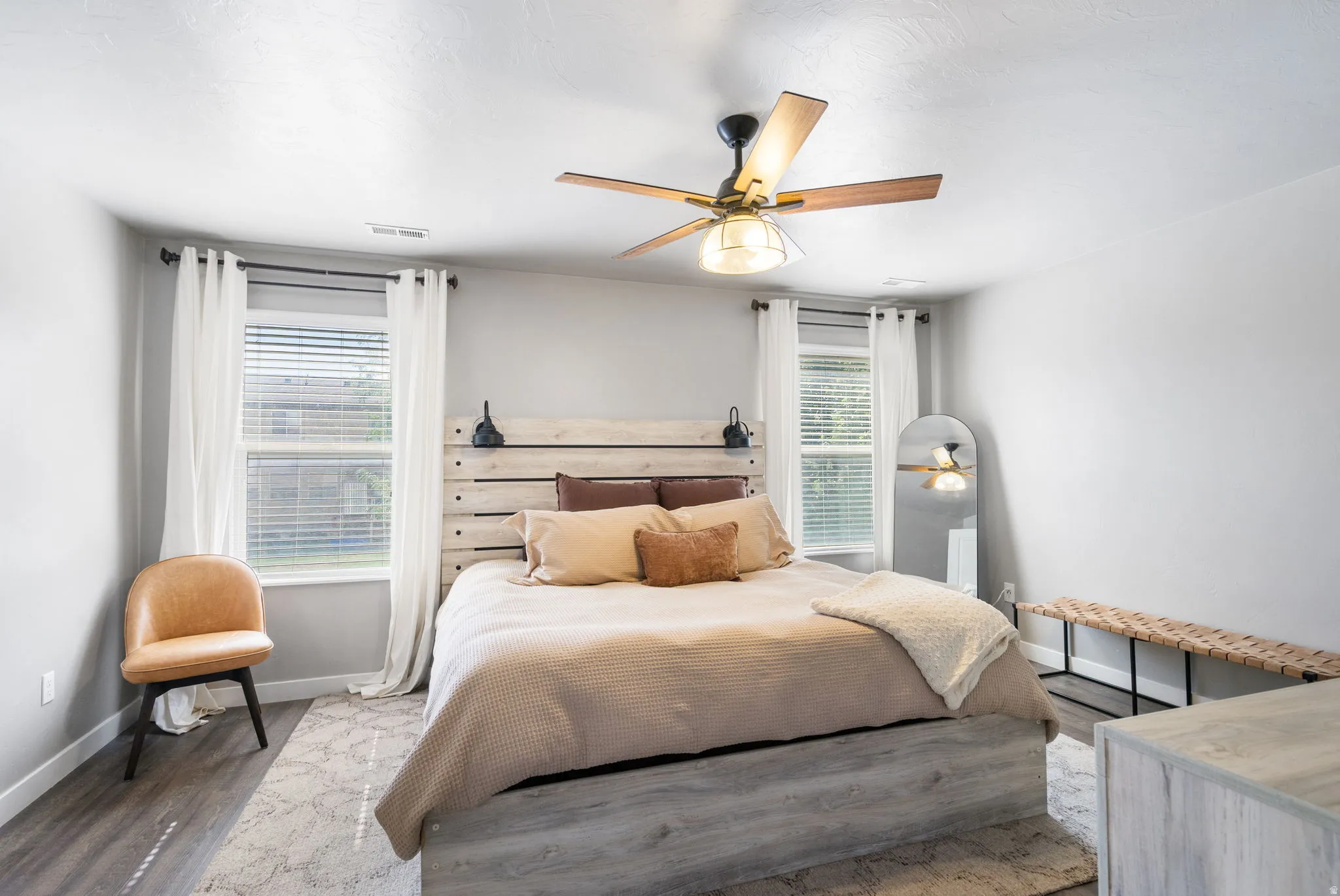 Two windows with blinds, wood-finish flooring, and a ceiling fan with integrated lighting