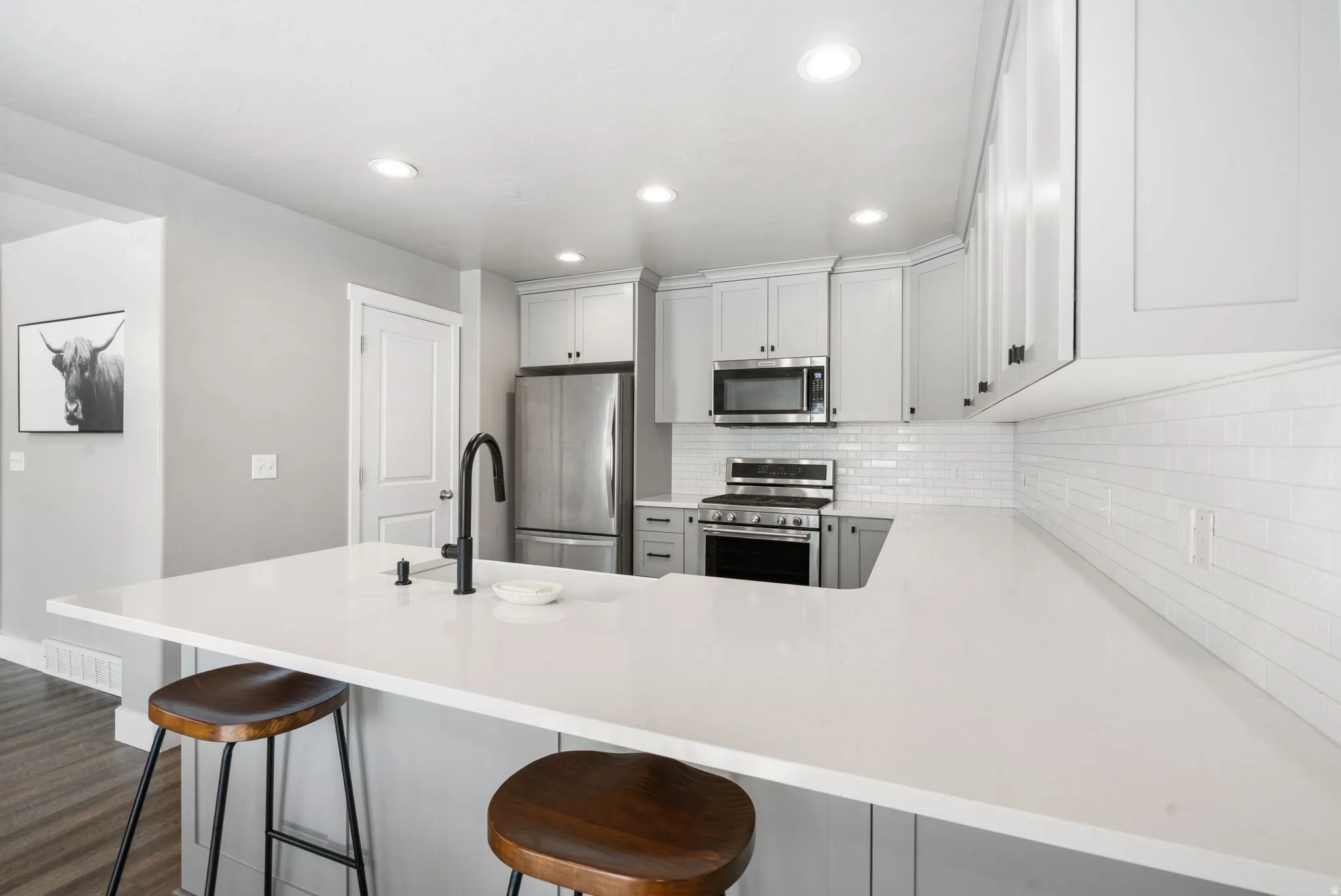 Modern kitchen featuring light gray cabinetry, a white subway tile backsplash, stainless steel appliances, and a solid surface countertop with an integrated sink and matte black faucet