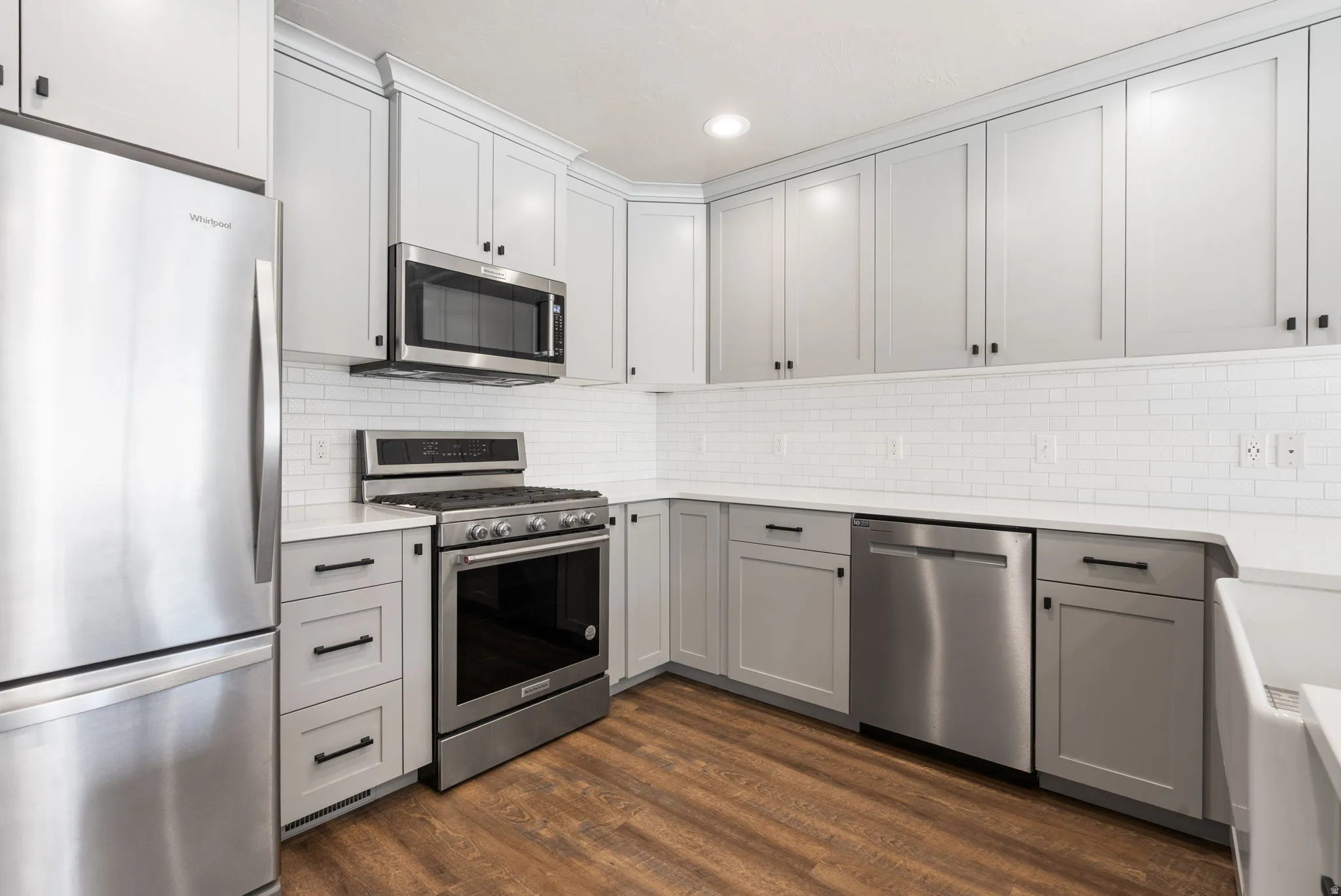 Kitchen featuring light gray cabinetry, stainless steel appliances, white subway tile backsplash, white countertops, and wood-finish flooring