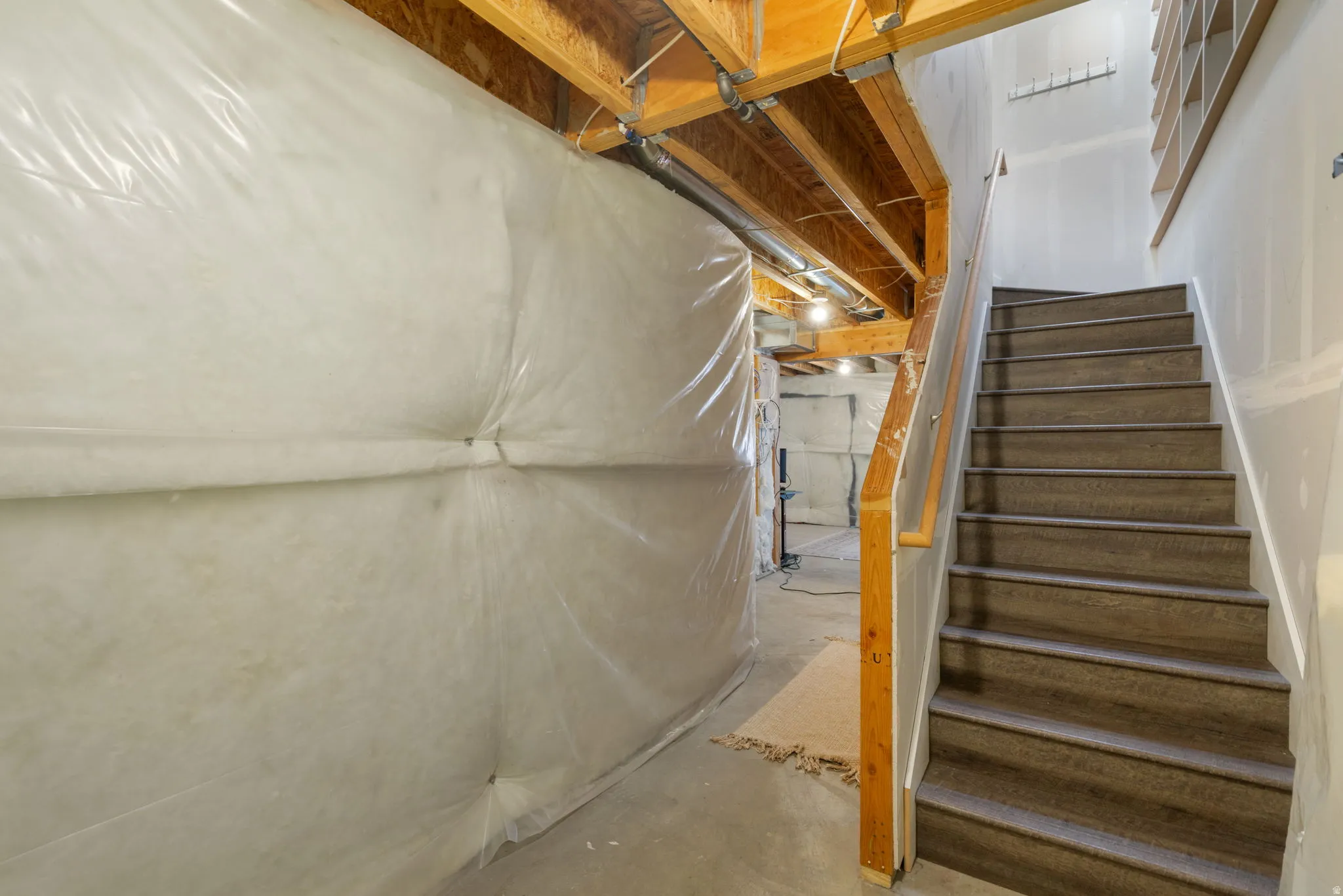 Unfinished basement space featuring exposed wood joists, a wooden staircase with carpeted treads, and partial wall insulation