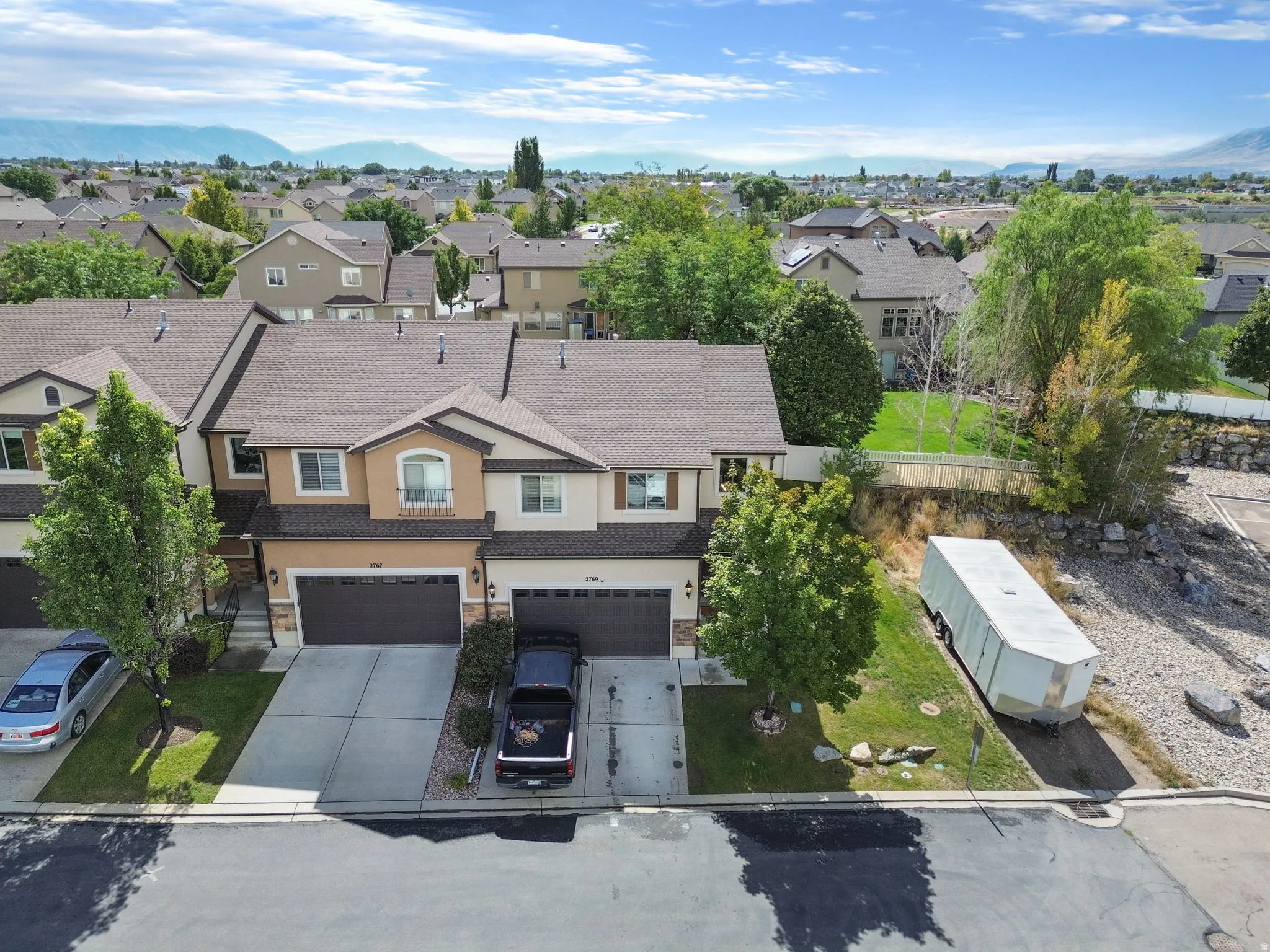 Two-story townhome with a two-car garage, concrete driveway, and a front yard with mature trees