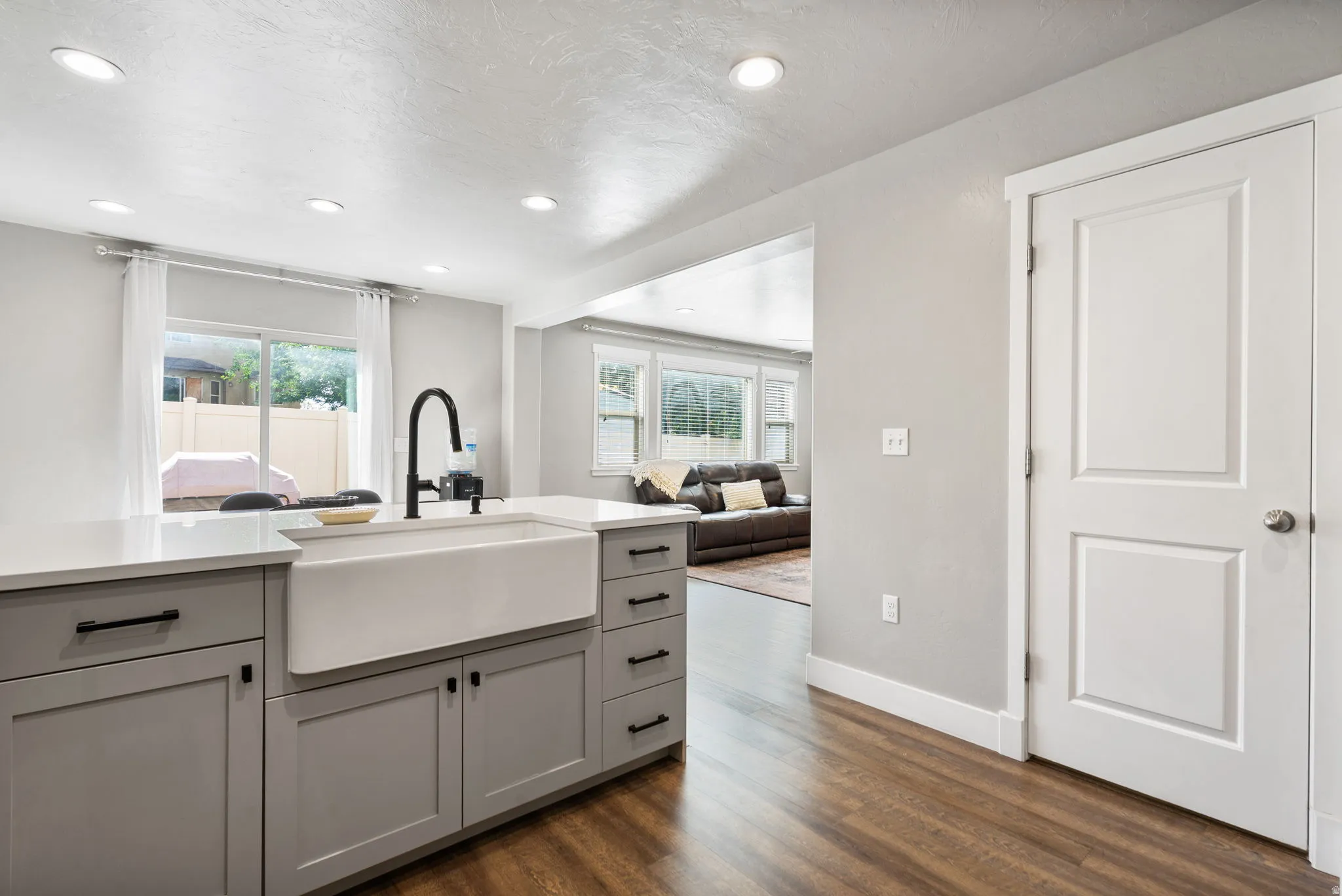 Kitchen island with a white farmhouse sink, matte black gooseneck faucet, light gray cabinetry, and white countertops