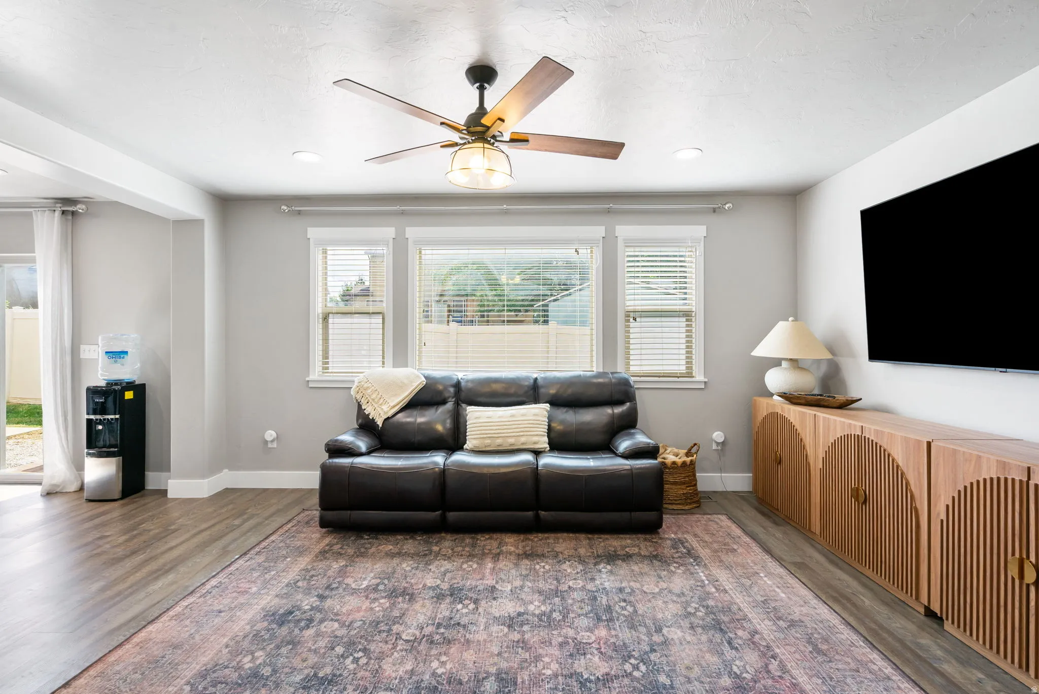 Wood-finish flooring, recessed lighting, ceiling fan, multiple windows with blinds, and white trim