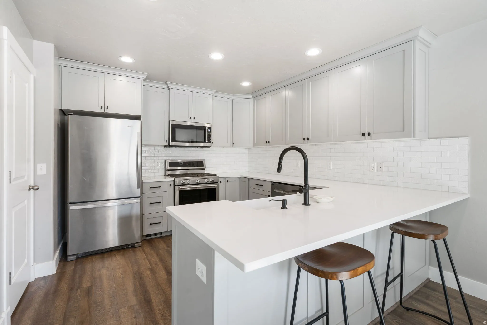 Modern kitchen featuring light gray cabinetry, stainless steel appliances, a white subway tile backsplash, white countertops, and wood-finish flooring
