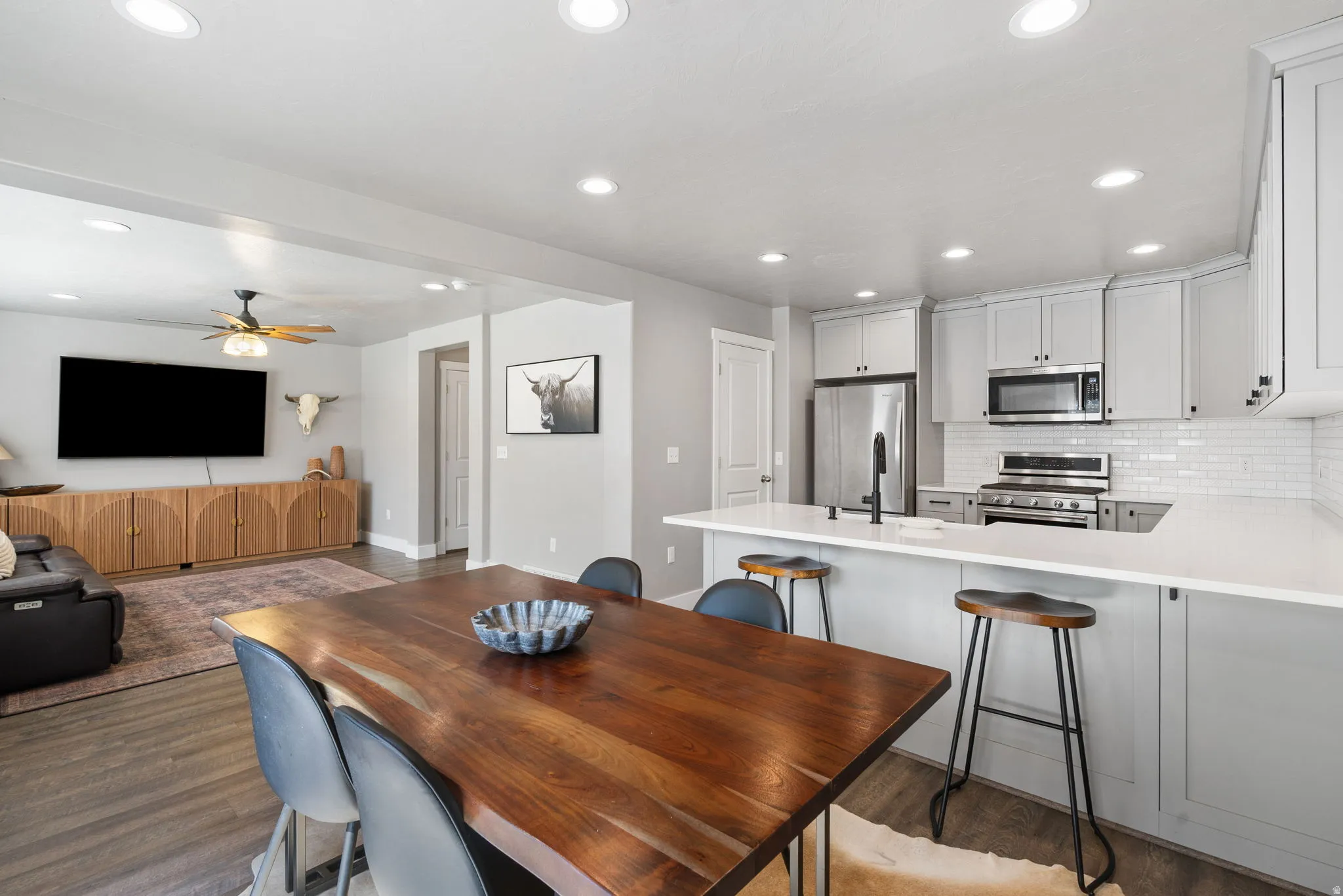 Open-concept living space featuring a kitchen island with seating, stainless steel appliances, light gray cabinetry, subway tile backsplash, and recessed lighting throughout