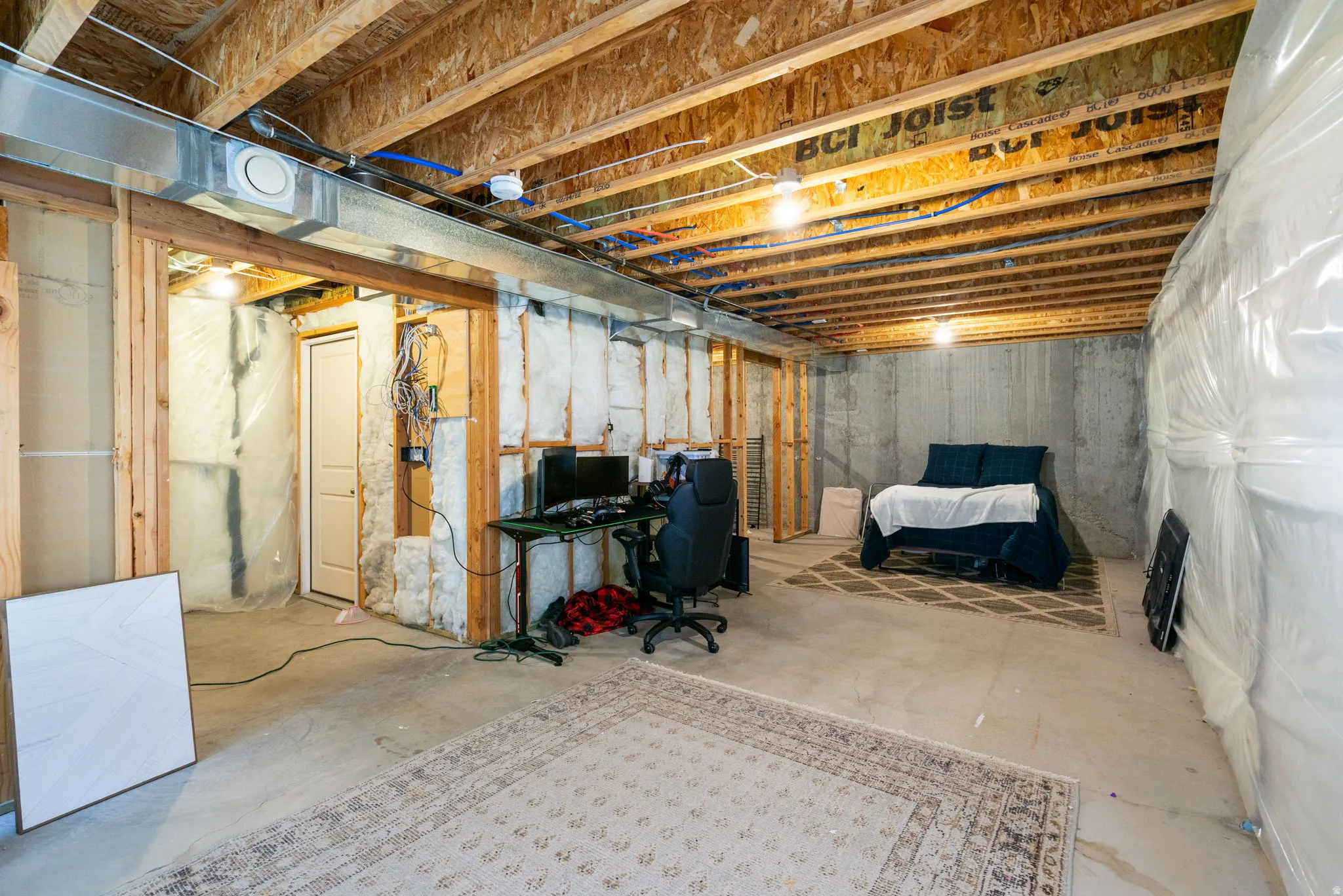 Unfinished basement with exposed wood joists, concrete foundation walls, and framed interior walls