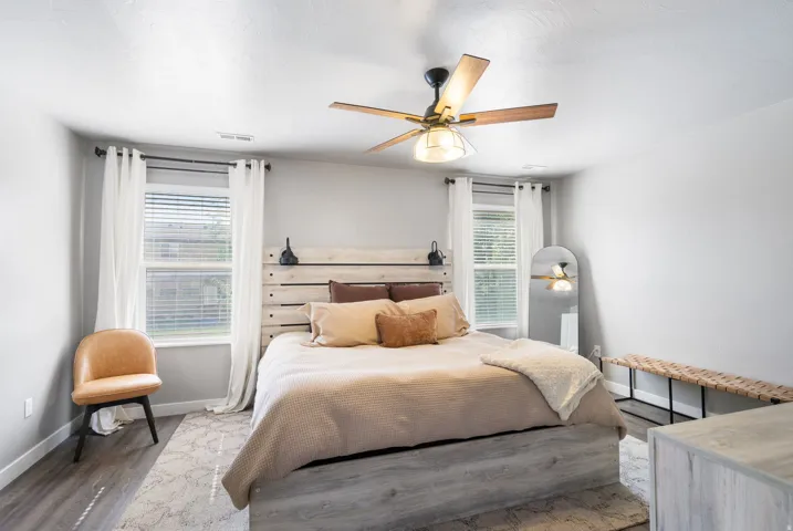 Two windows with blinds, wood-finish flooring, and a ceiling fan with integrated lighting