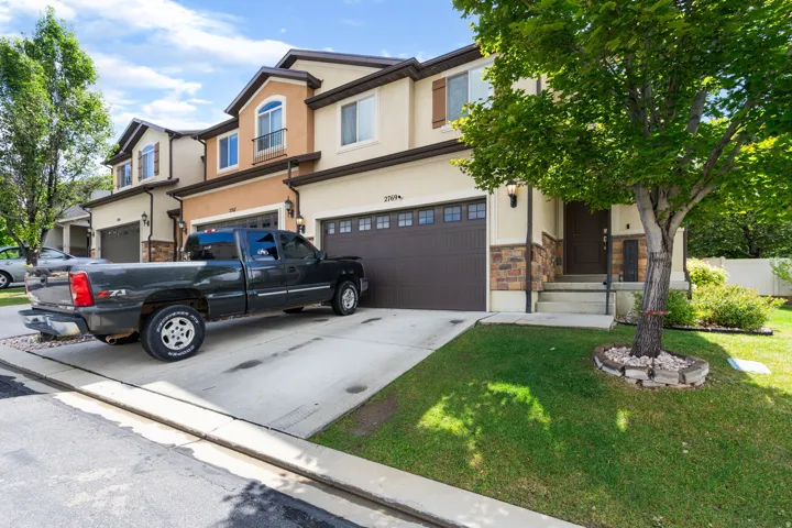 Two-story stucco and stone exterior, attached garage, concrete driveway, covered porch entry, and mature landscaping