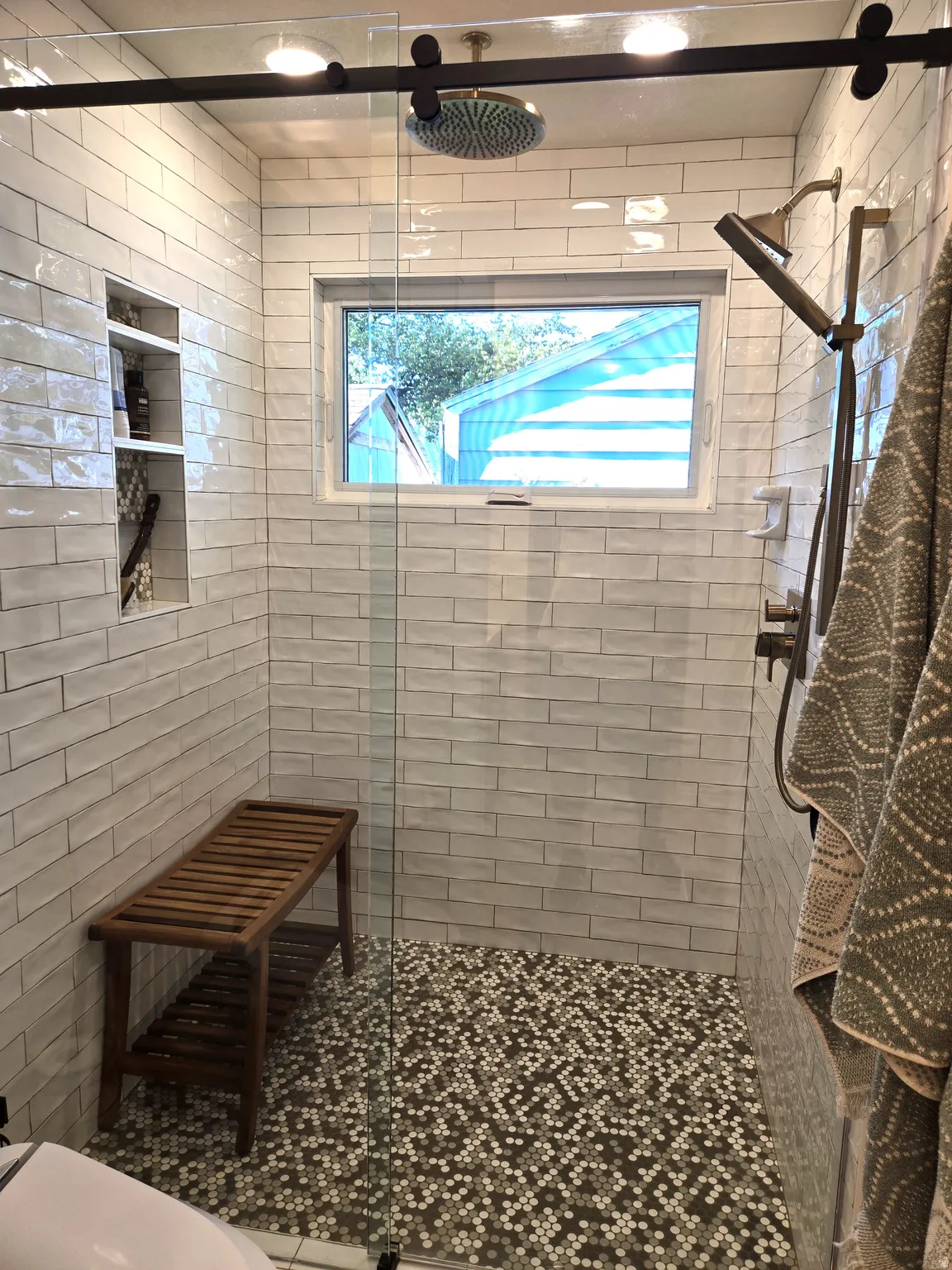 Glass-enclosed shower with white subway tile walls, mosaic tile flooring, a built-in shower niche, and a rain shower head