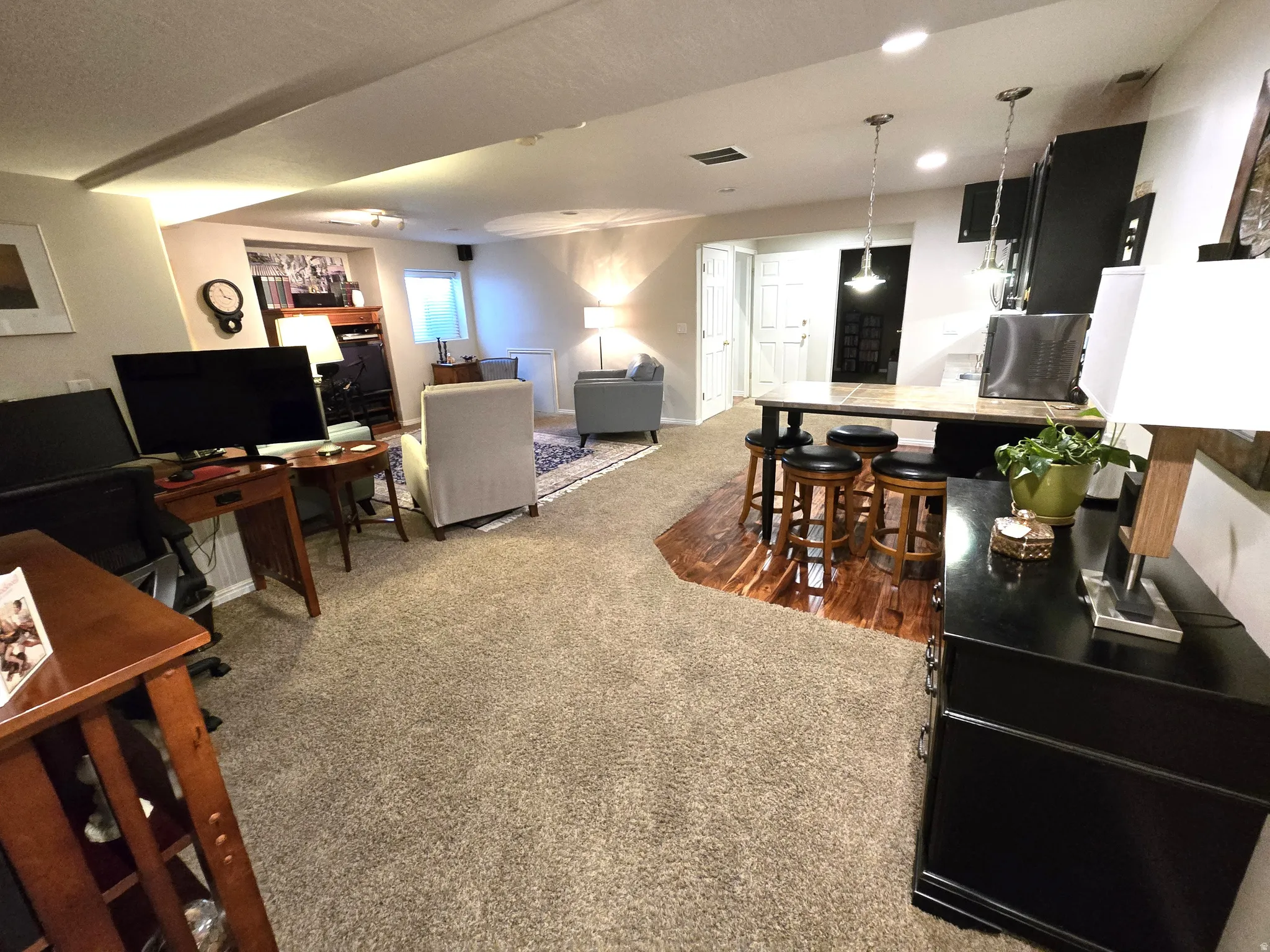 Open-concept living space with recessed lighting, carpeted and wood-finish flooring, and a built-in breakfast bar with pendant lighting