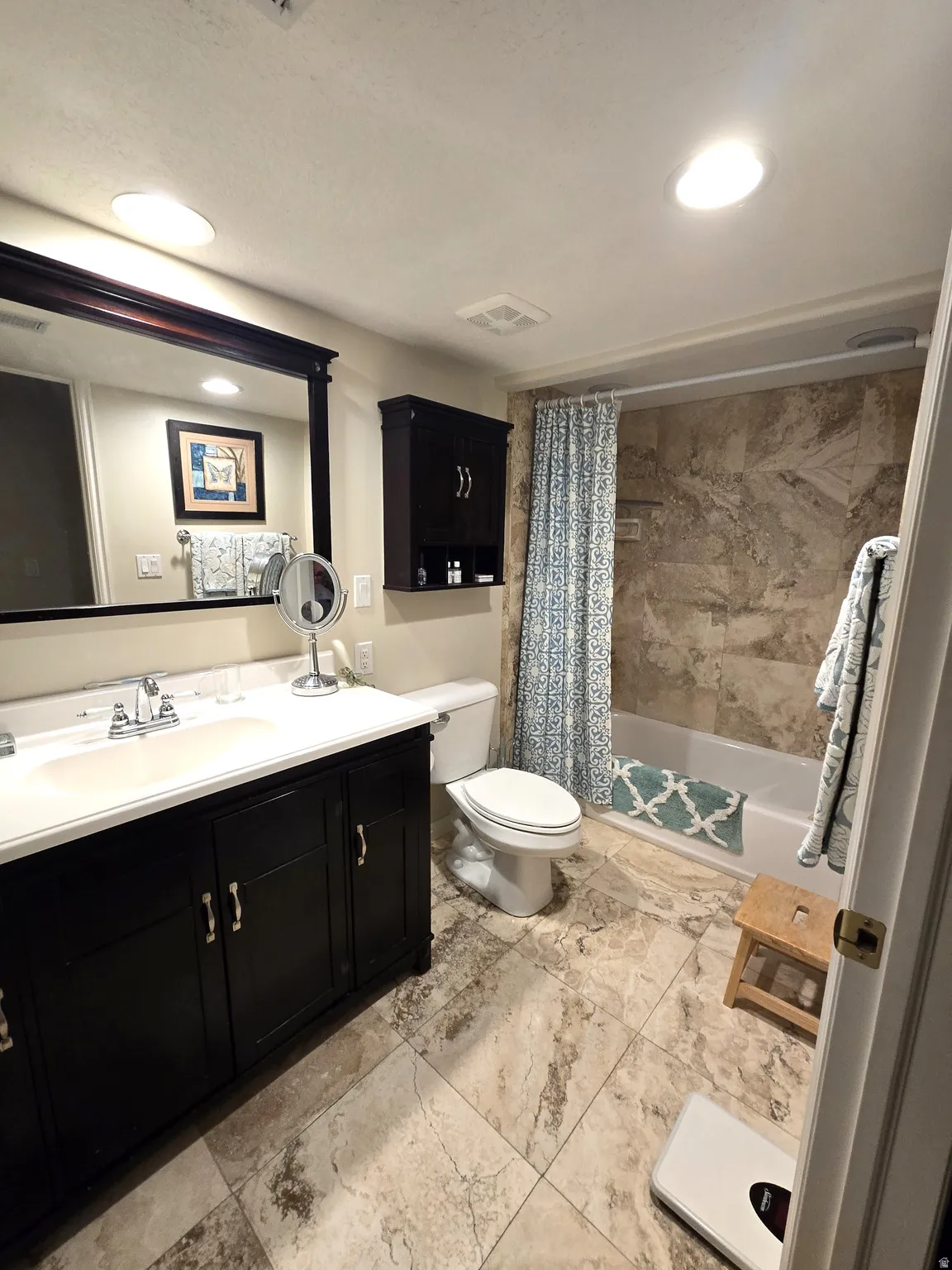 Vanity with an integrated sink and dark wood-finish cabinetry, a framed mirror, a built-in tub with a tiled surround, and large-format tile flooring