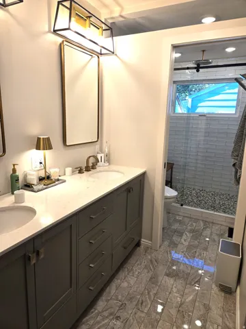 Double vanity with undermount sinks and brass-finish fixtures, ample cabinetry, stone-finish countertop, rectangular vanity mirrors, and integrated lighting