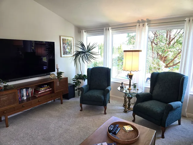 Vaulted ceiling, expansive windows with white trim, wall-to-wall carpeting, and a built-in media console