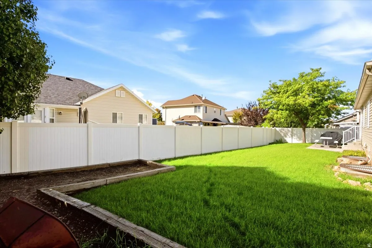 Expansive backyard featuring a green lawn, white privacy fencing, and a built-in planter box