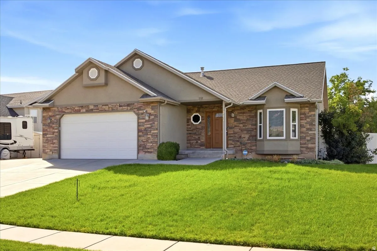 Stucco exterior with stone accent facade, attached garage with white door, wood entry door with circular window, bay window, and a gabled roof
