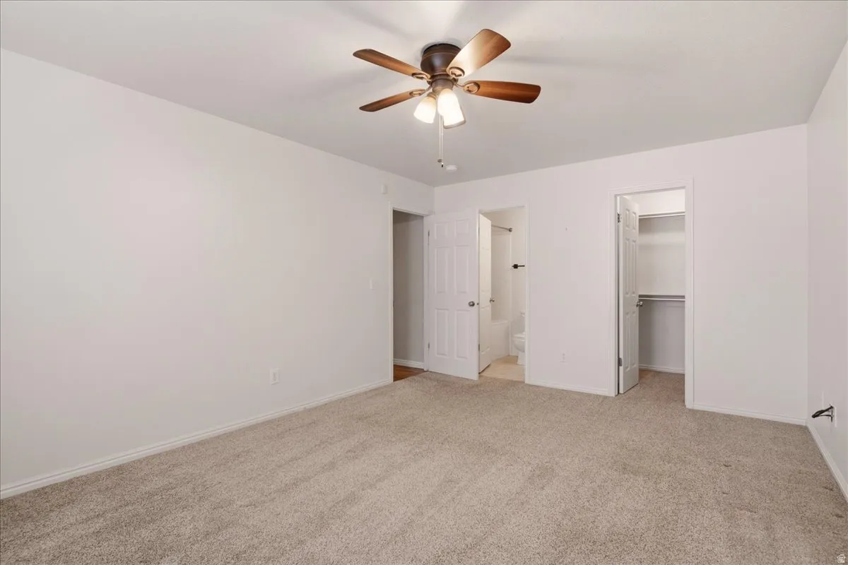 Neutral tone wall paint, textured carpet flooring, ceiling fan with integrated lighting, bi-fold closet doors, and recessed closet shelving