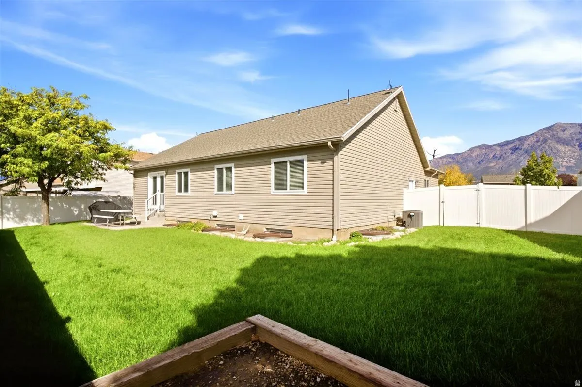Expansive backyard featuring a manicured lawn, established tree, concrete patio, and white vinyl fencing