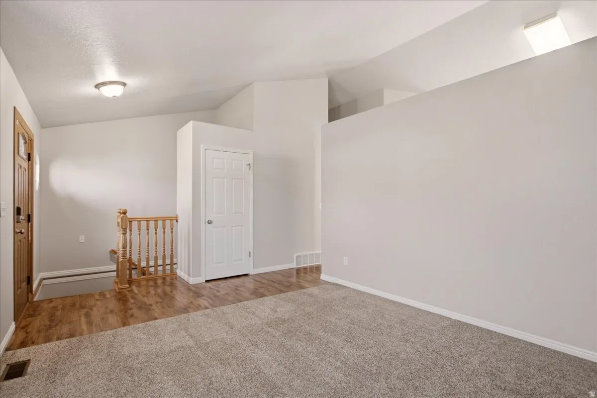Vaulted ceiling with an overhead light fixture, light-toned carpeting, wood-finish flooring, and a natural wood staircase with balusters