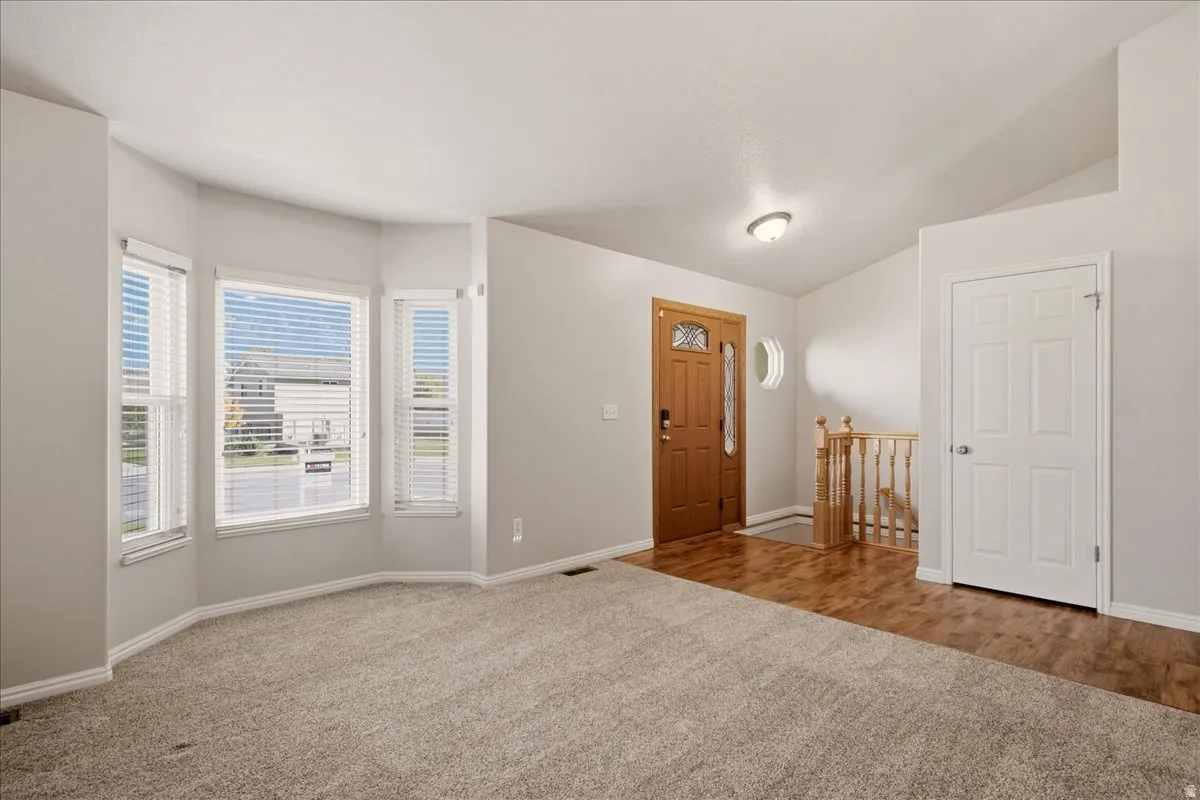 Bay window with blinds, wood-finish flooring, staircase with wooden railing, paneled interior door, and a wooden front entry door