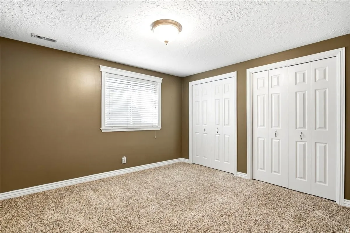 Plush carpet flooring, neutral paint tones, window with white blinds, white trim, and two bifold closet doors