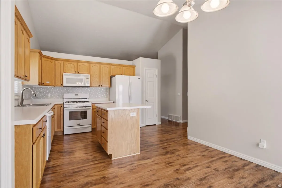 Vaulted ceilings, wood-finish flooring, light wood cabinetry, white countertops, and a kitchen island with built-in storage