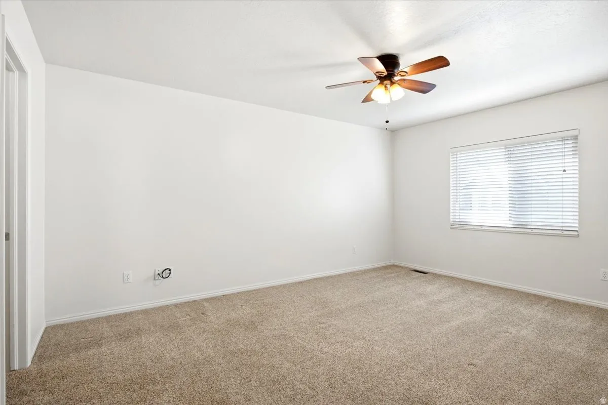 Carpeted flooring, white walls, window with blinds, ceiling fan with integrated lighting, and a white door frame