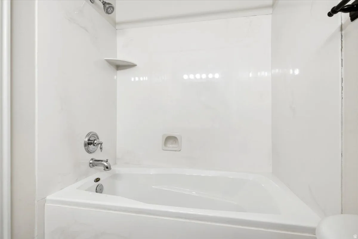White bathtub with integrated shower, chrome fixtures, and a corner shelf