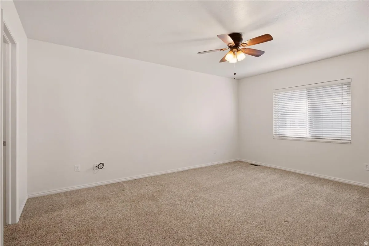 Carpeted room featuring a ceiling fan with integrated lighting and a window with blinds